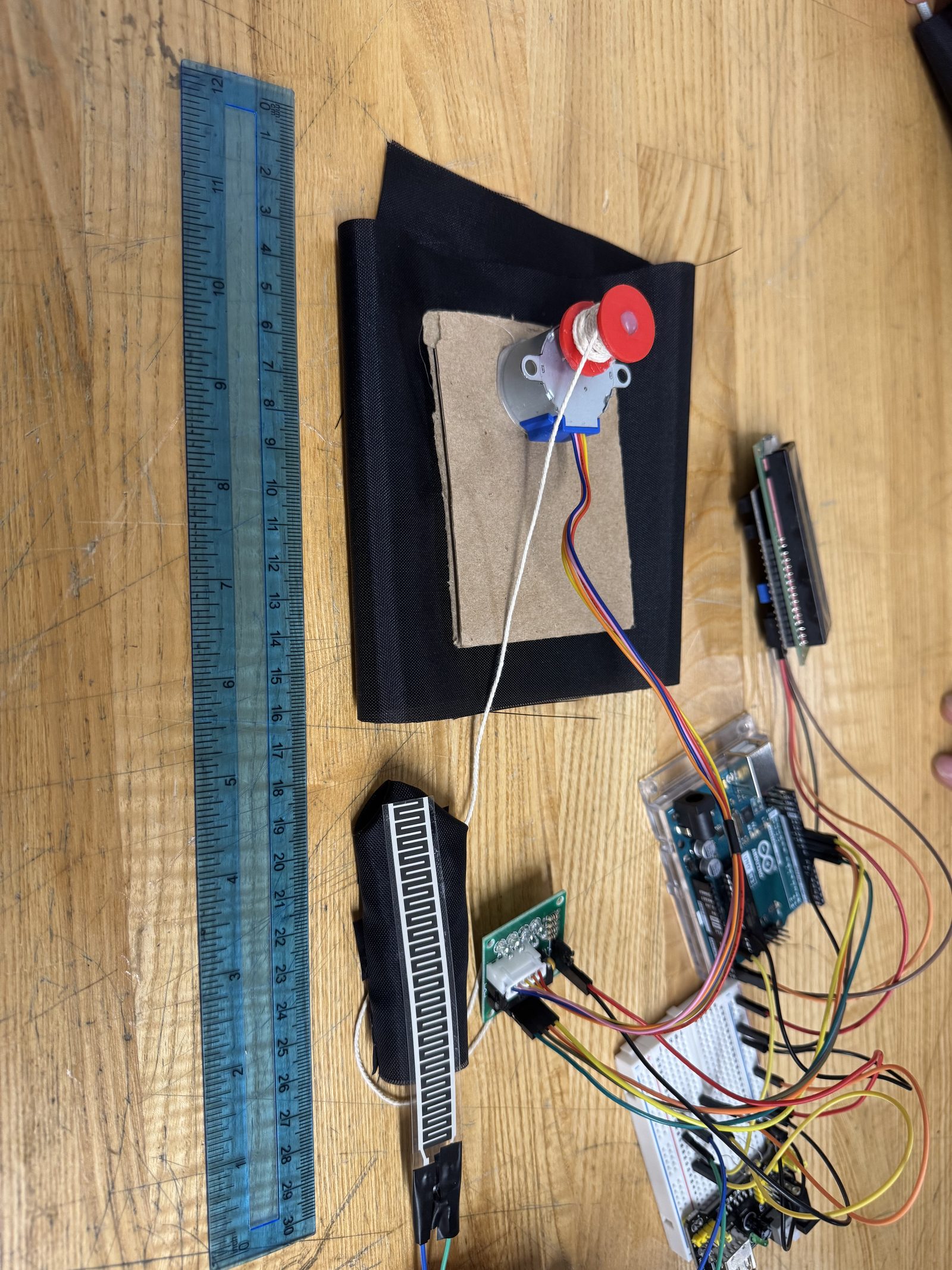 Early fin-ray gripper prototype with a stepper motor, cardboard structure, and flex sensor on a breadboard